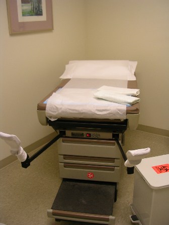 A gynecological exam table waiting to be boarded, stirrups out and up, for positioning the legs in the utmost open wide position. 